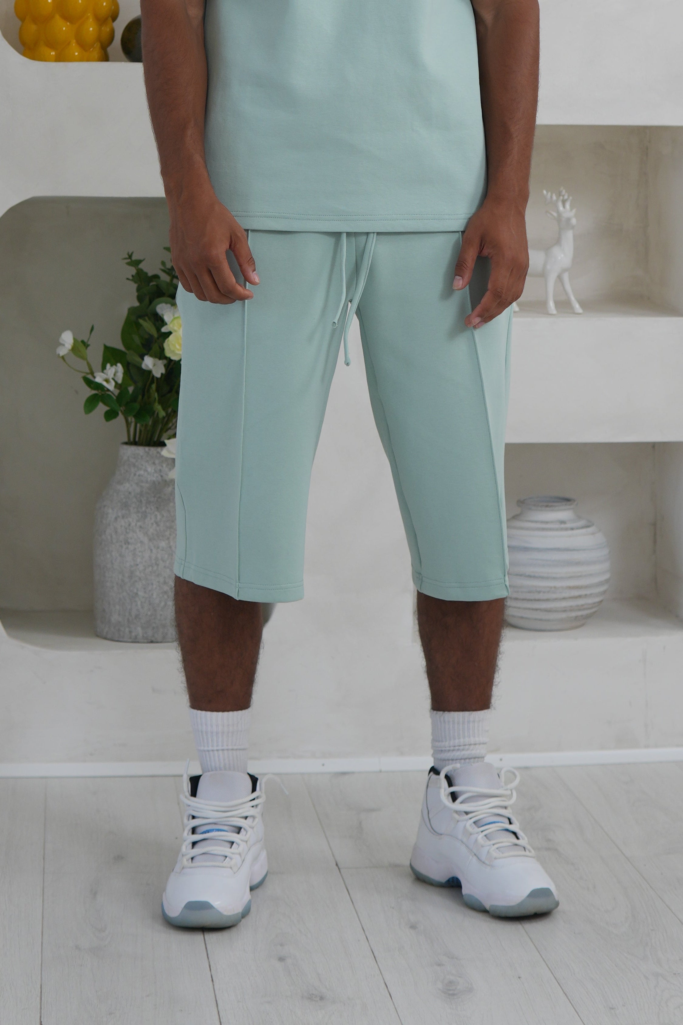 Person wearing a sage green outfit standing in a modern indoor setting with geometric shapes.