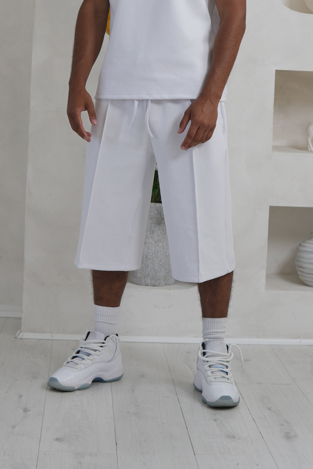 Person wearing a white outfit standing in a minimalistic room with light-colored floor and walls. Knee Length Shorts YAZIR