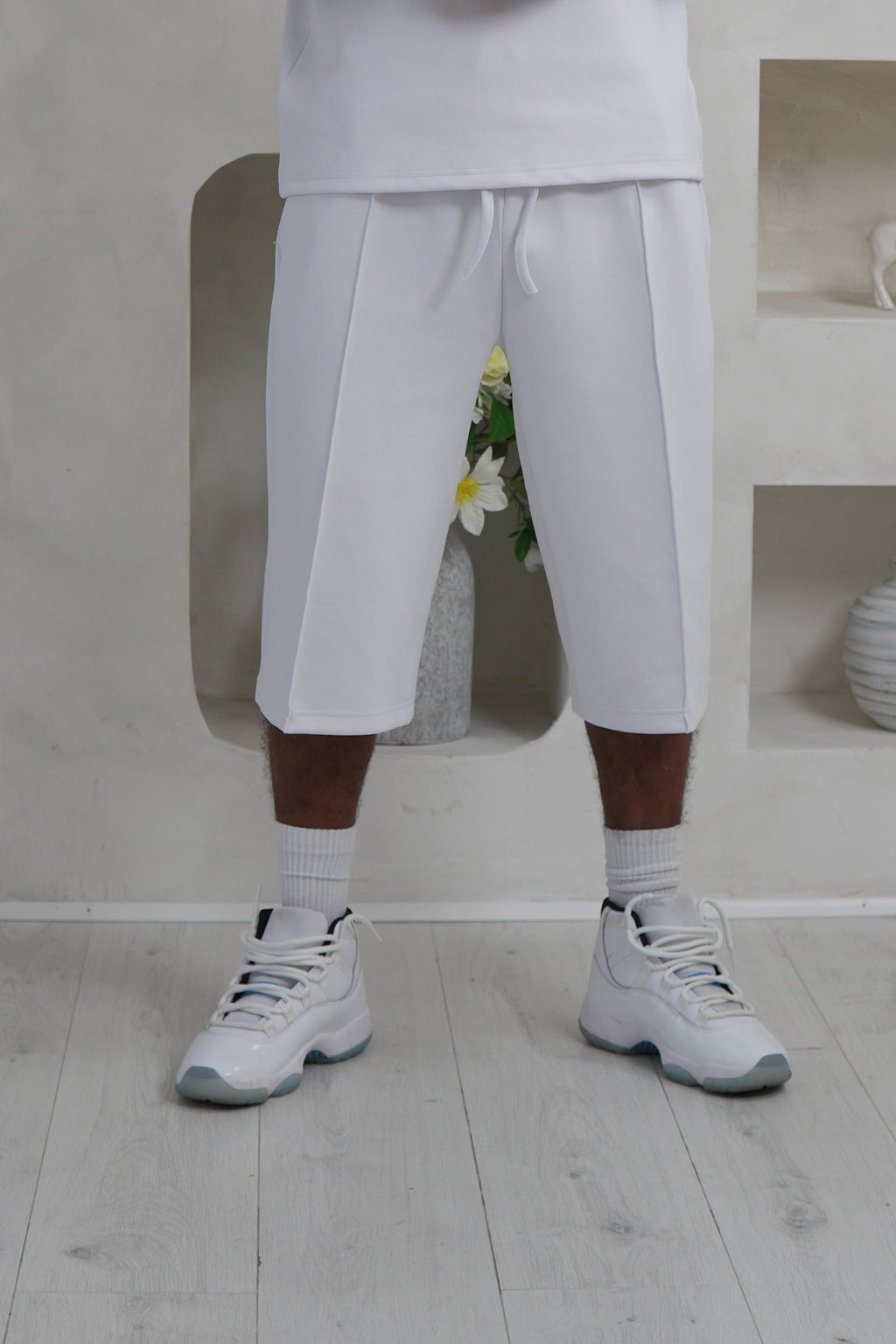 Person in a white outfit standing in a minimalist room with light-colored floor and walls. Knee Length Shorts YAZIR