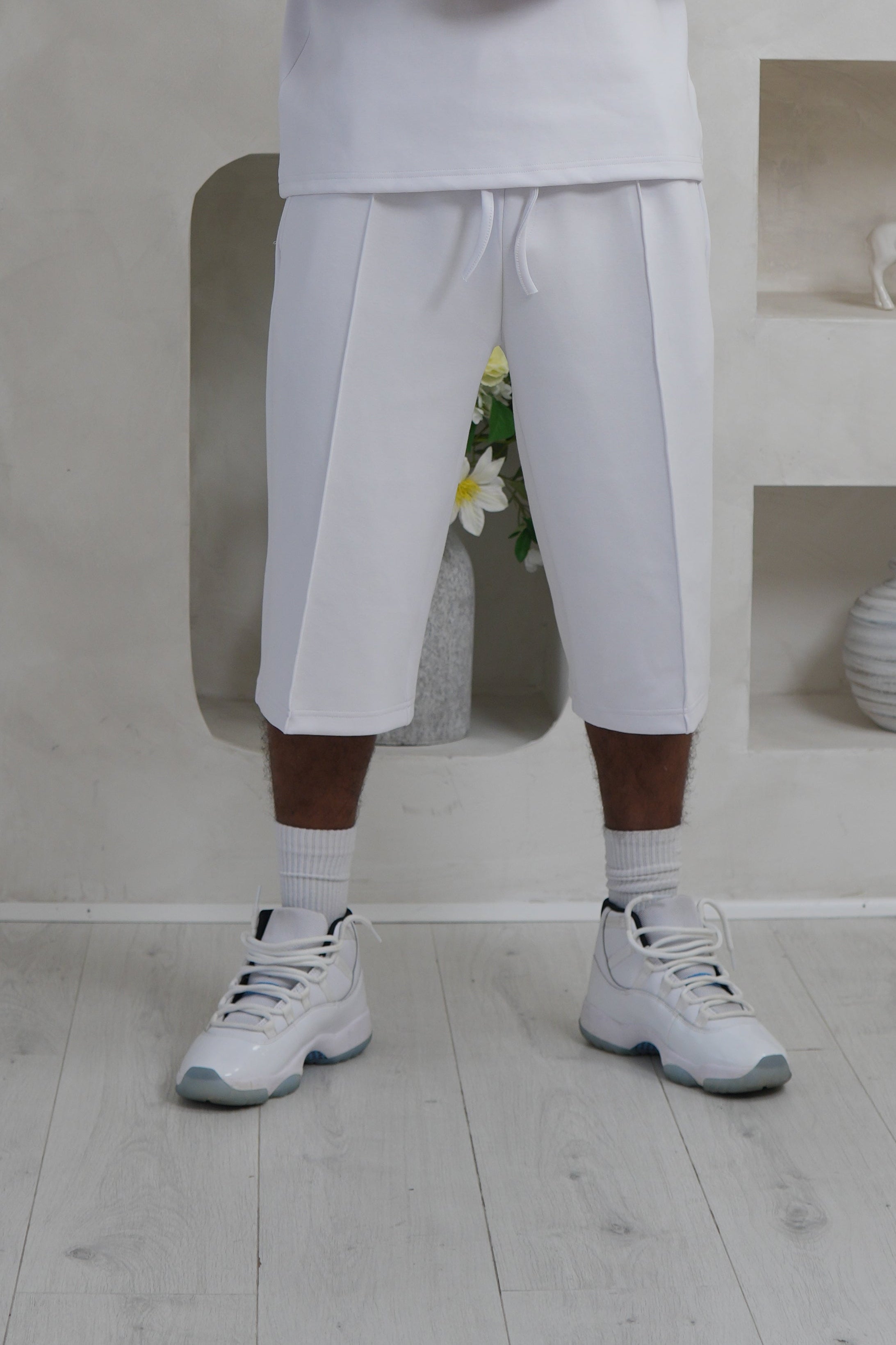 Person in a white outfit standing in a minimalist room with light-colored floor and walls. Knee Length Shorts YAZIR