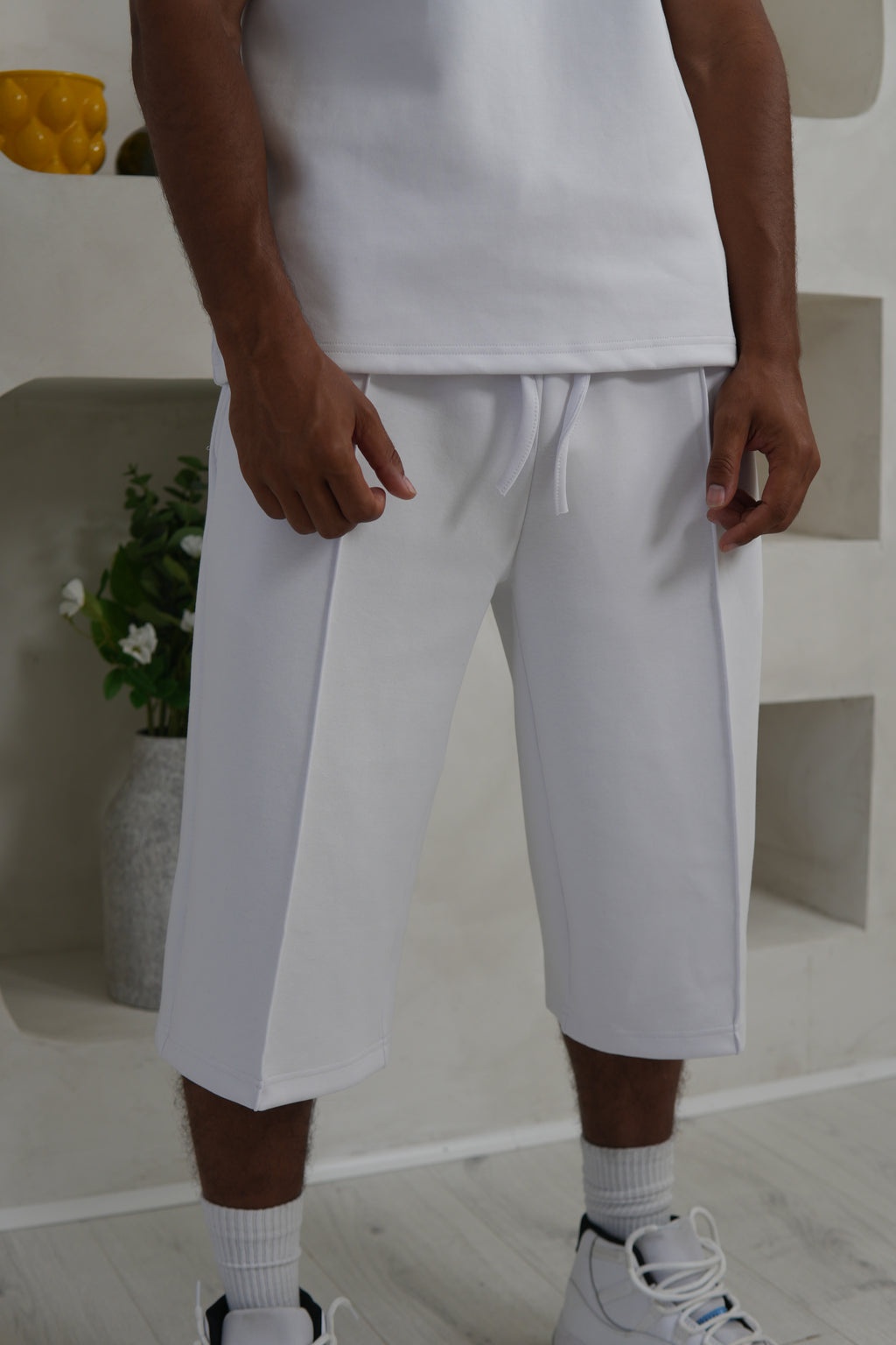 Person wearing white pants and sneakers in a minimal indoor setting. Knee Length Shorts YAZIR
