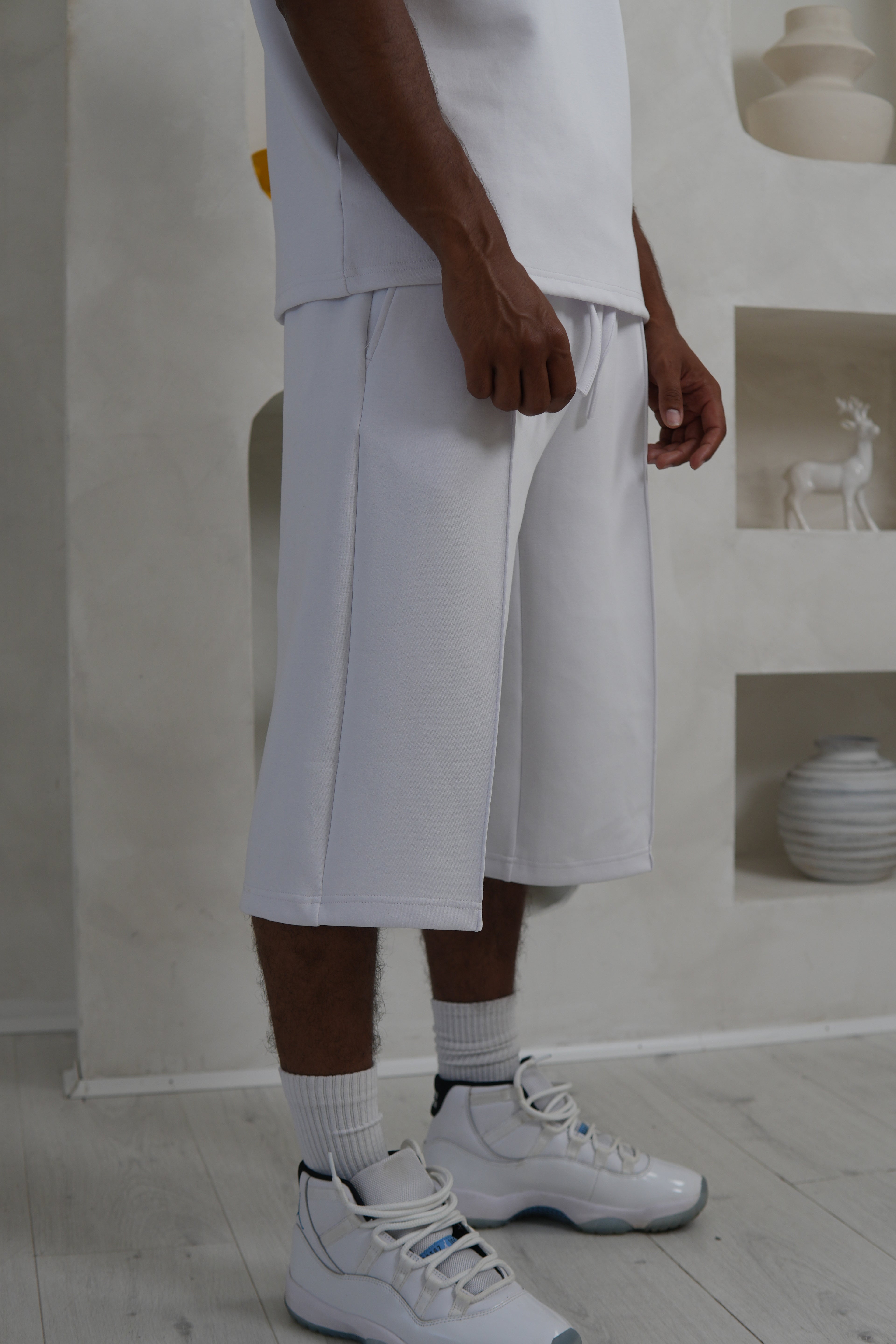 Person wearing white shorts and sneakers in a minimal indoor setting Knee Length Shorts YAZIR