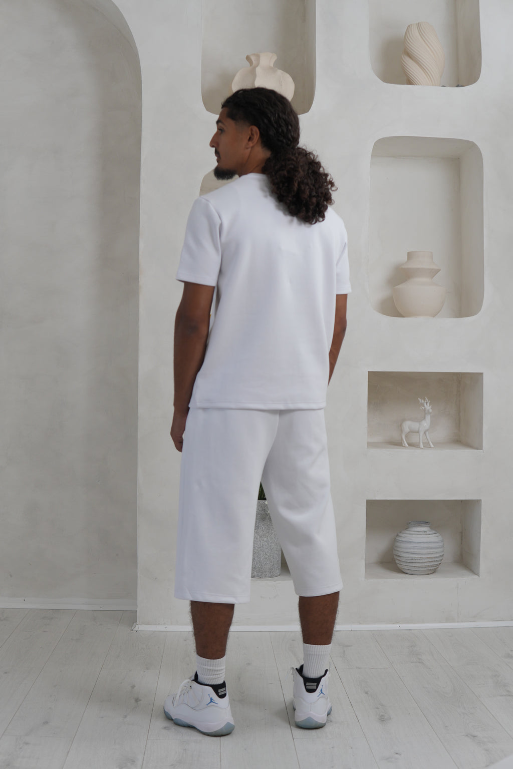Person wearing a white outfit standing in a minimalistic room with sculptures. Knee Length Shorts YAZIR