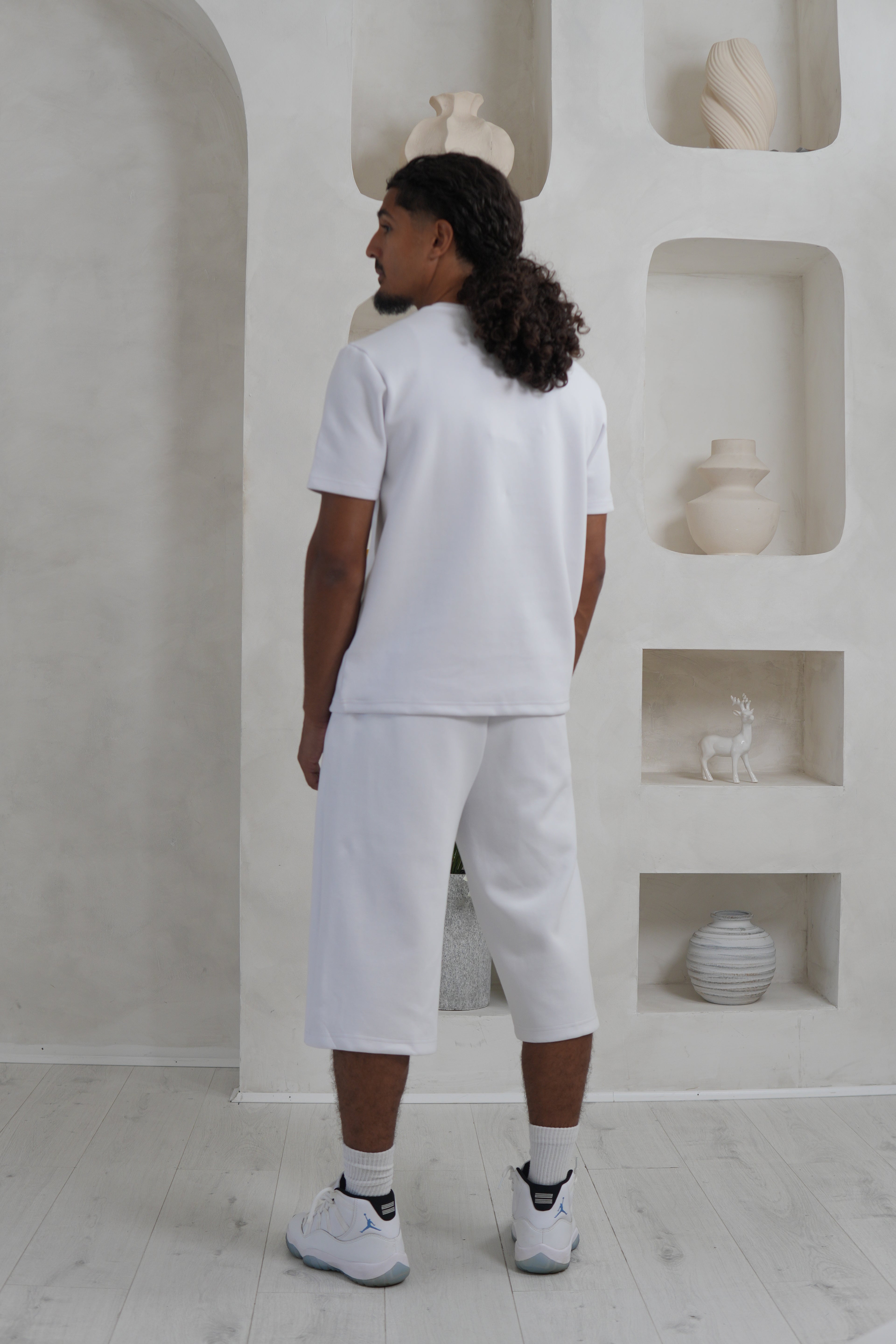 Person wearing a white outfit standing in a minimalistic room with sculptures. Knee Length Shorts YAZIR