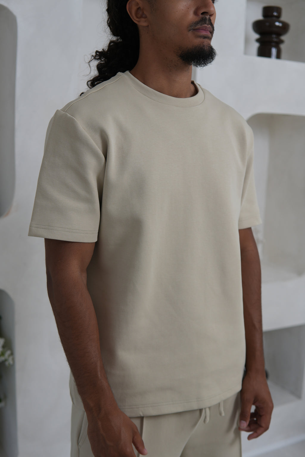 Man wearing a beige t-shirt and pants in a minimal indoor setting