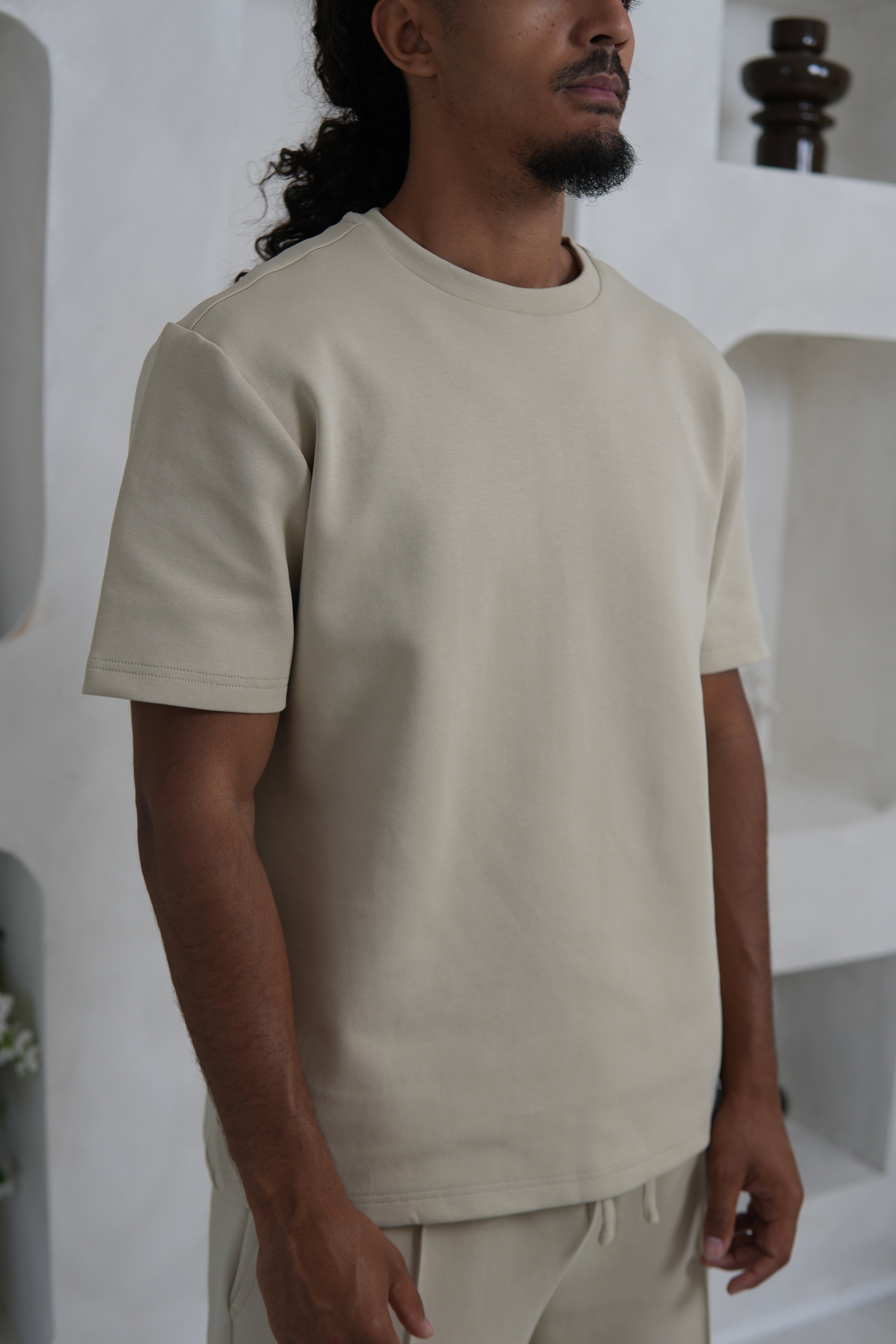 Man wearing a beige t-shirt and pants in a minimal indoor setting