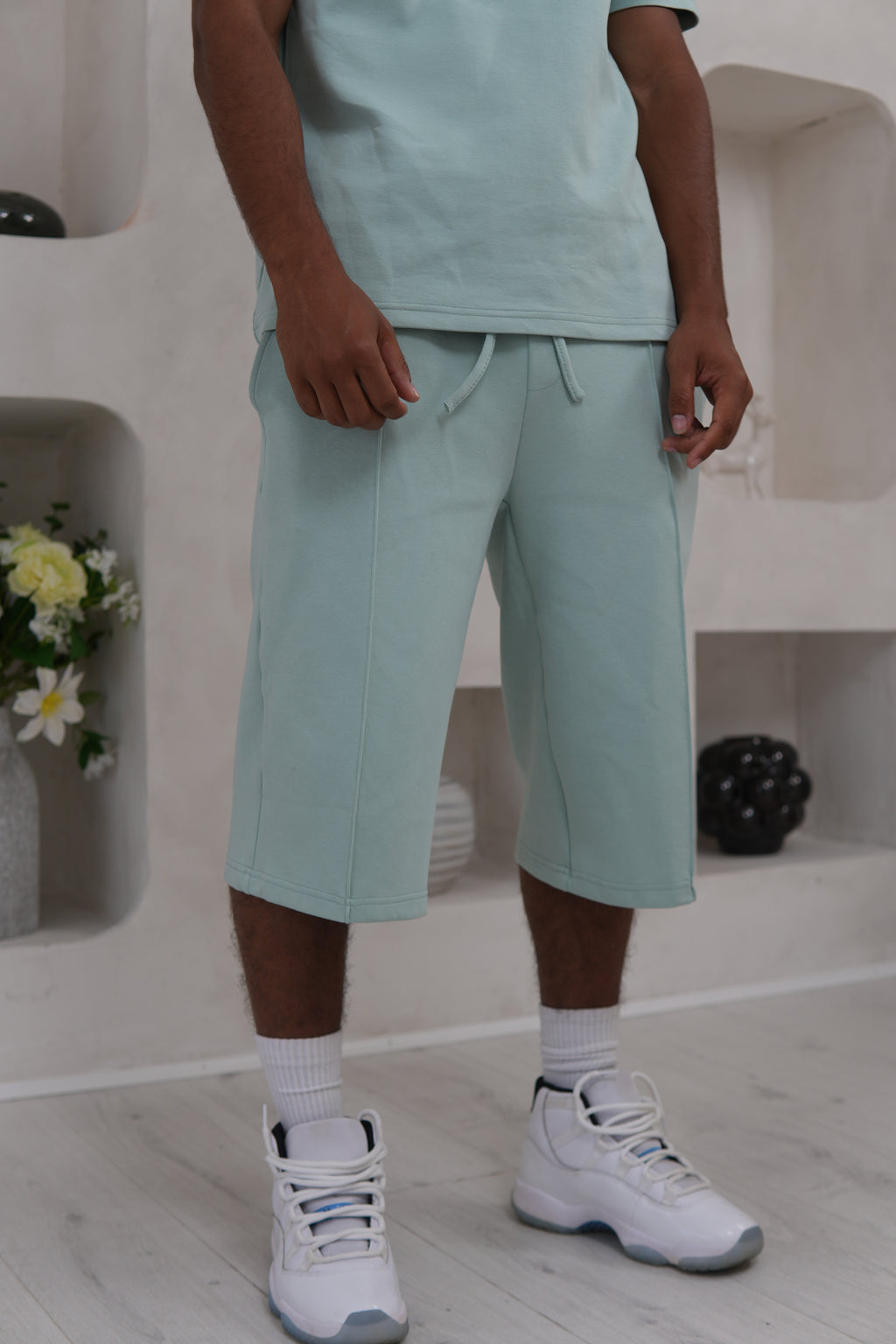 Person wearing sage green pants and white sneakers in a minimal indoor setting.