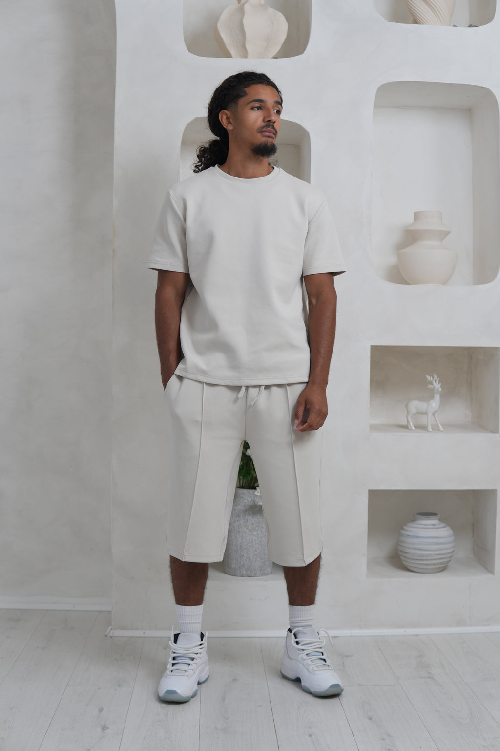 Person wearing a white outfit standing in a minimalistic room with white walls and floor.