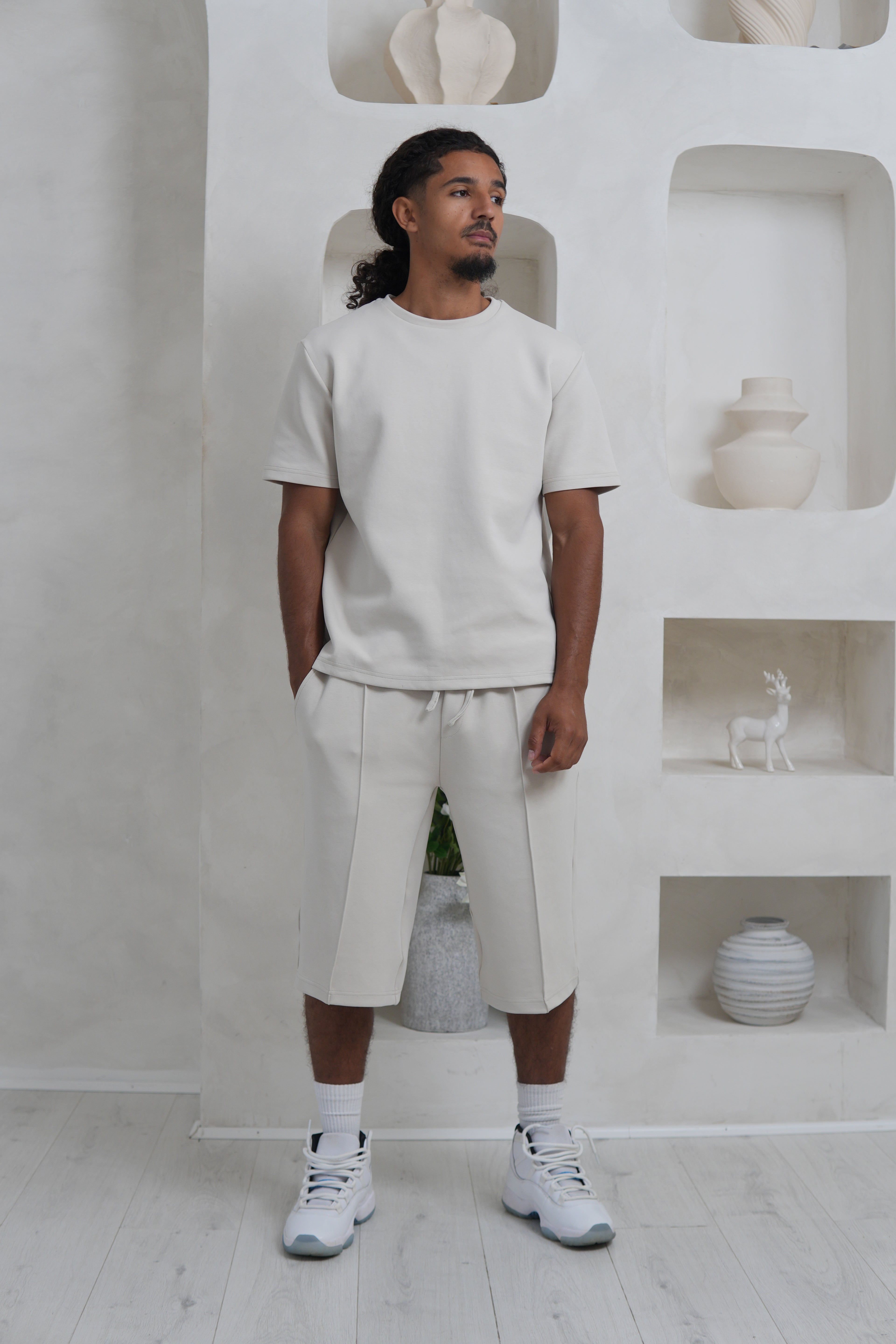 Person wearing a white outfit standing in a minimalistic room with white walls and floor.