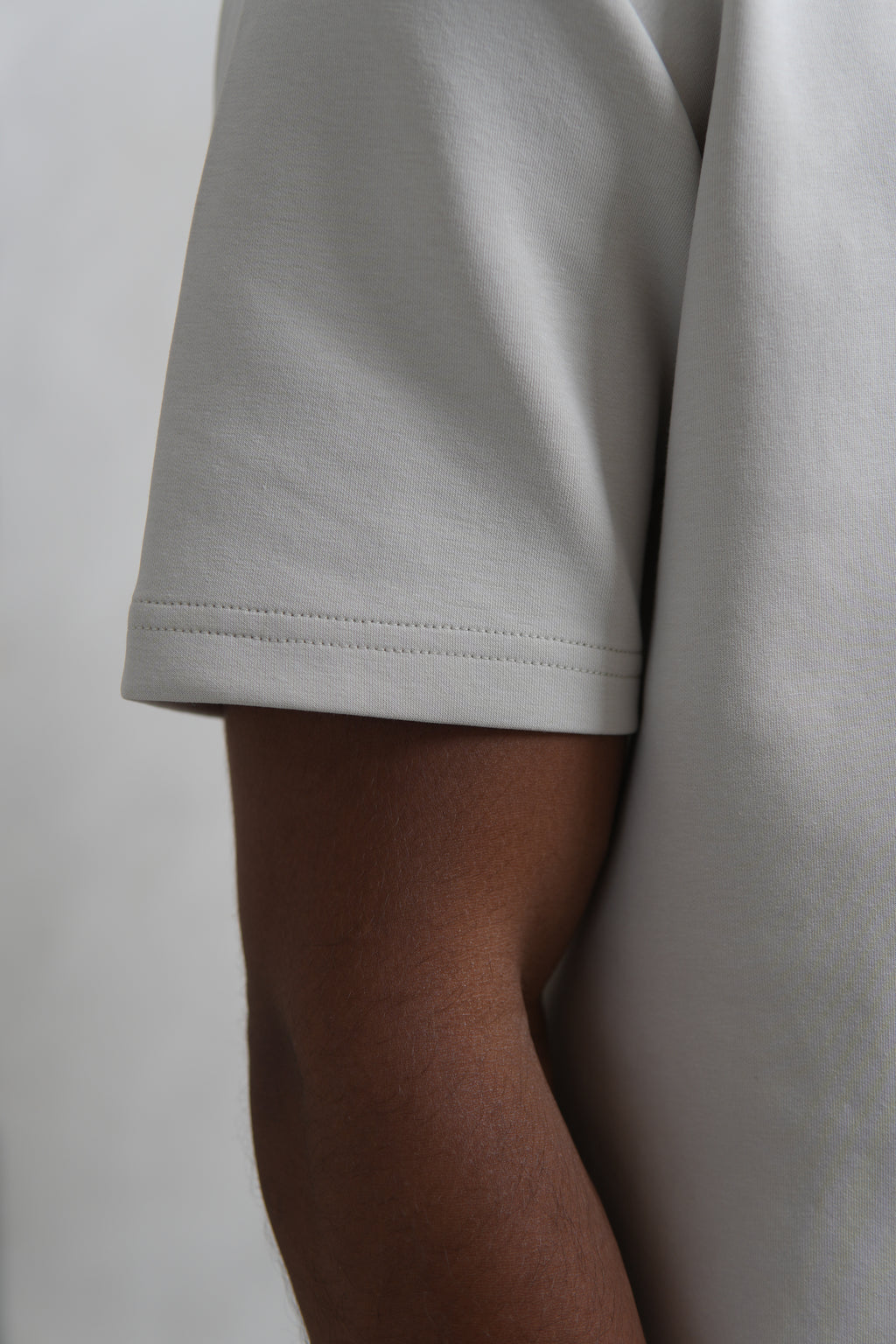 Close-up of a person wearing a light gray t-shirt against a plain background YAZIR