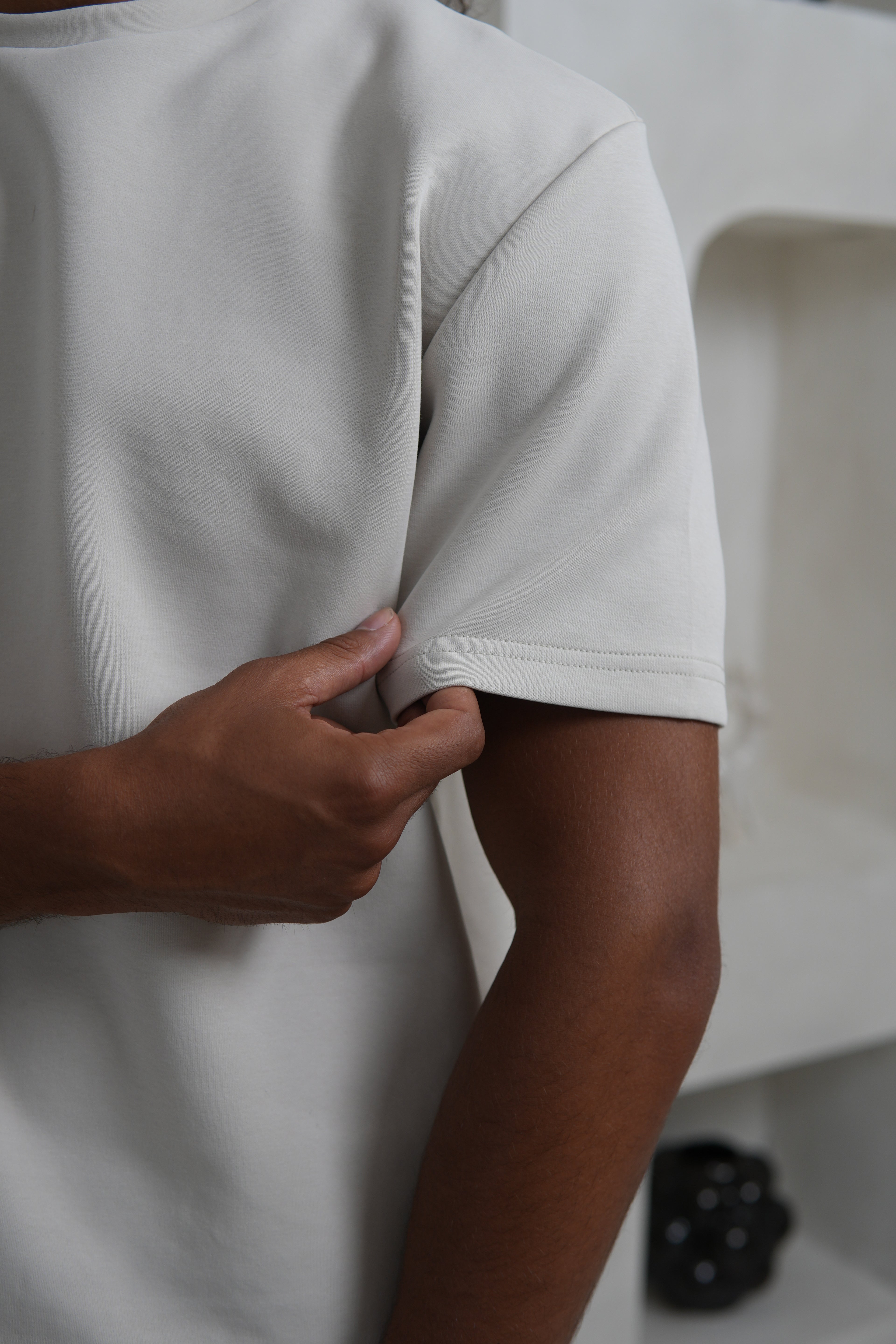 Person wearing a plain white t-shirt with a hand adjusting the sleeve. YAZIR